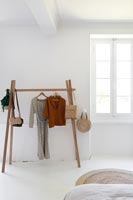 Simple wooden clothes rail in white painted country bedroom 