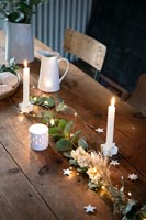 Fairy lights and candles on wooden dining table at Christmas time 