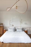 White bed on floor of country bedroom with unusual lampshade on pendant light