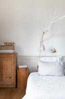 Lamp and wooden bird suspended from painted branch over bed 