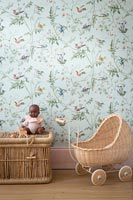 Wicker pram, toy dolly and basket in childrens room with floral wallpaper 