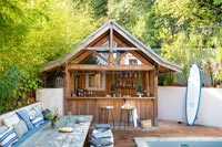 Wooden bar and large wooden table in courtyard garden with swimming pool 