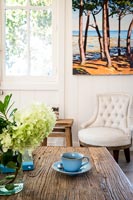 Cup and saucer wooden coffee table with colourful painting on wall 
