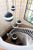 View down curving staircase with modern pendant lights and stained glass window 