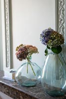 Cut flowers in large glass vases on marble mantelpiece 
