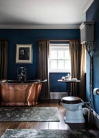 Copper roll top bath in dark blue bathroom 
