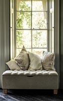 Upholstered ottoman as window seat in country bedroom 