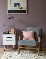 Purple painted wall behind armchair and cabinet 