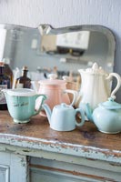 Pastel coloured teapots and jugs on distressed sideboard 