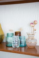 Vase of dried roses and glass jars on wooden shelf  