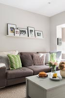 Modern sitting room with display of family photographs on shelf above sofa 