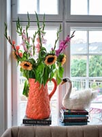 Bright orange jug vase full of flowers on windowsill 