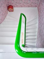 View down white staircase with green painted bannister and pink wall paper 