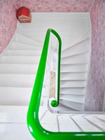 View down white staircase with green painted bannister and pink wall paper 