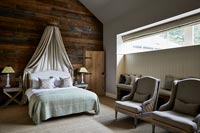 Country bedroom with wooden feature wall and canopy over bed 