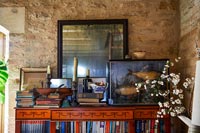 Artwork, ornaments and books on ornate bookcase against stone wall 