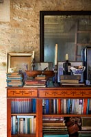 Artwork, ornaments and books on ornate bookcase against stone wall 