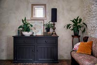 Black wooden sideboard in country living room with bare plaster wall