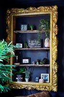 Shelves framed with gilded picture frame on black painted wall 