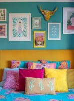 Display of framed paintings on colourful bedroom wall 