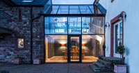 Country house exterior with modern glazed joining room illuminated in evening 