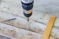 Woman using an electric screwdriver to drive long screws through the boards
