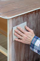 Woman using sandpaper to prepare the set of drawers for painting
