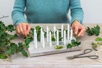 Woman decorating candle plinth with holy, ivy and moss