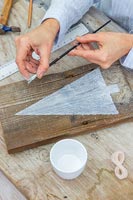 Woman using a paint brush to flick paint onto wood to simulate snow falling