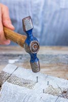 Close up detail of woman using hammer to nail small tacks into wooden board 