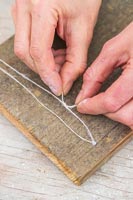 Woman making wall hanging on the back of a piece of wooden board with string