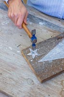 Woman fixing painted wooden stars onto board using a hammer and small tack
