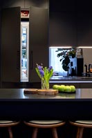 View to open integrated refrigerator across island in modern black kitchen 