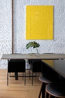 Modern dining room with white painted brickwork wall and yellow artwork