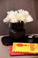 Black vase with white cut flowers on bedside table with reading material 