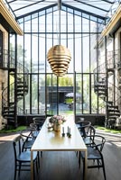 Contemporary dining room in glazed building with metal spiral staircases on both sides and view to garden