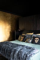 Black and gold bedroom with fur throw and skull patterned cushions on bed 
