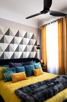 Modern bedroom with patterned feature wall colourful bedding and black ceiling fan 
