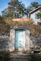 Rustic entrance gate set in drystone wall with rusty signage above 