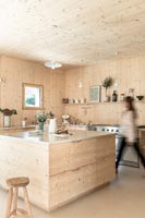 Woman walking through modern timber clad kitchen 