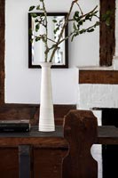 Long white vase with tree branches as arrangement in country dining room 