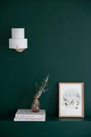 Small white sconce light above shelf on green painted wall 