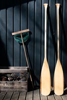 Oars and a fishing net next to crate of pine cones on decking 
