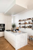 Island in modern kitchen with wooden shelving and parquet flooring 