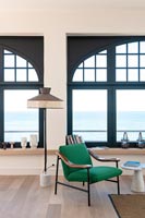 Green armchair and vintage standard lamp next to large windows with sea views 