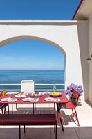Red dining table laid for lunch on terrace with sea views 