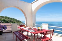 Red dining table laid for lunch on terrace with sea views in summer 