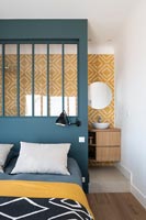 Modern bedroom with grey painted dividing wall and yellow patterned tiling in en-suite bathroom area 
