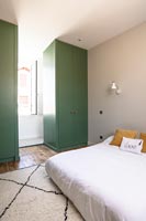 Green painted wardrobes either side of window in modern bedroom 