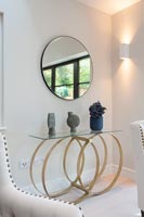 Unusual table with ornaments underneath a circular mirror and sconce light